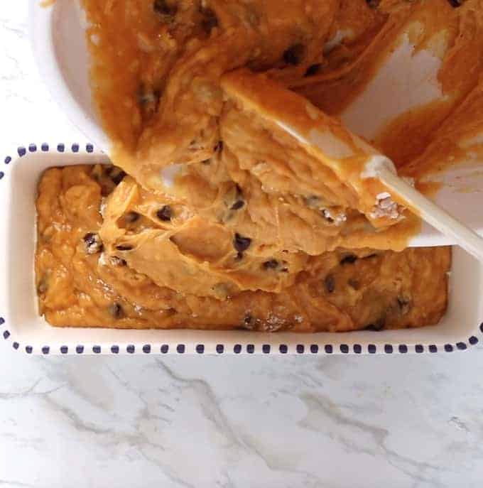Chocolate Chip Pumpkin Bread being made - the batter is being poured into a bread pan on a white table. 