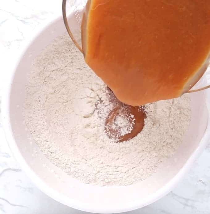 Chocolate Chip Pumpkin Bread being made - the wet ingredients are being poured into the dry ingredients in a white bowl on a white surface. 