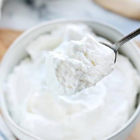 Stablilized whipped cream shown in a white bowl with a spoon scooping some out.