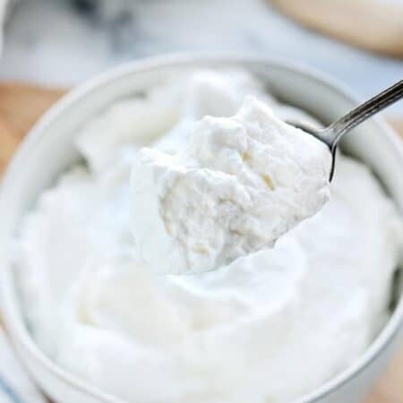 Stablilized whipped cream shown in a white bowl with a spoon scooping some out.