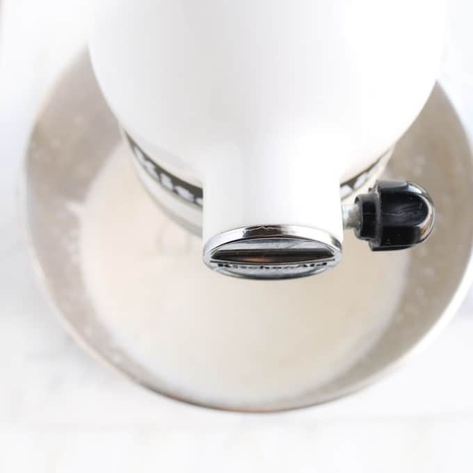 Crème à fouetter stabilisée en cours de fabrication, montrant une photo de haut en bas d'un mélangeur d'aide à la cuisine blanc fouettant de la crème à fouetter dans son bol en métal.