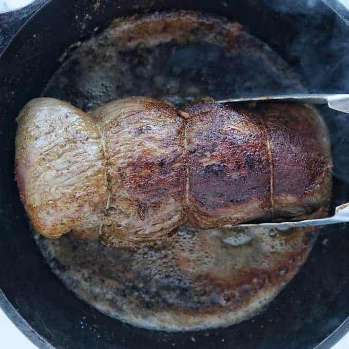 Whole Beef Tenderloin Steak being seared in a cast iron skillet, shown up close.