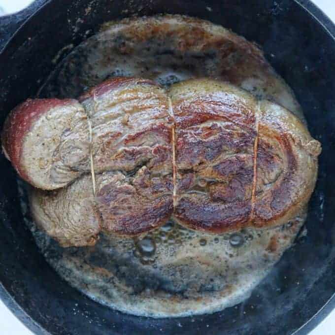 Beef Tenderloin shown in a black cast iron pan with the opposite side of the beef being seared so the side facing up has a golden brown sear. 