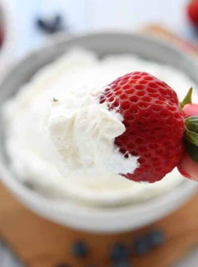 A close up of a bowl of whipped cream with a strawberry.