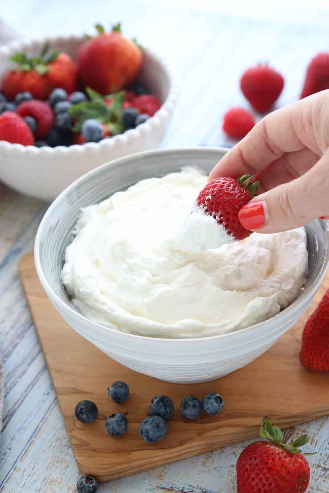 A bowl of whipped cream sitting on top of a wooden table with a strawberry