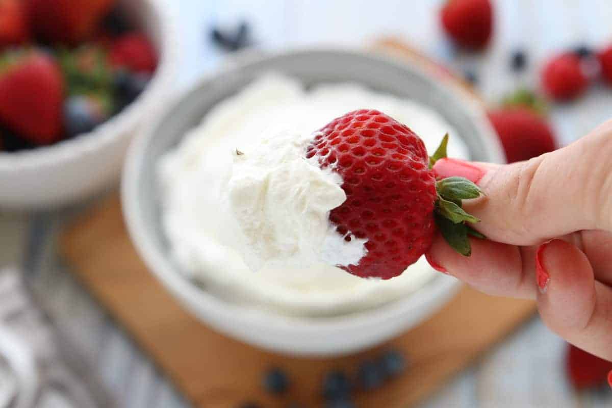 Un gros plan d'un bol de crème fouettée avec une fraise.
