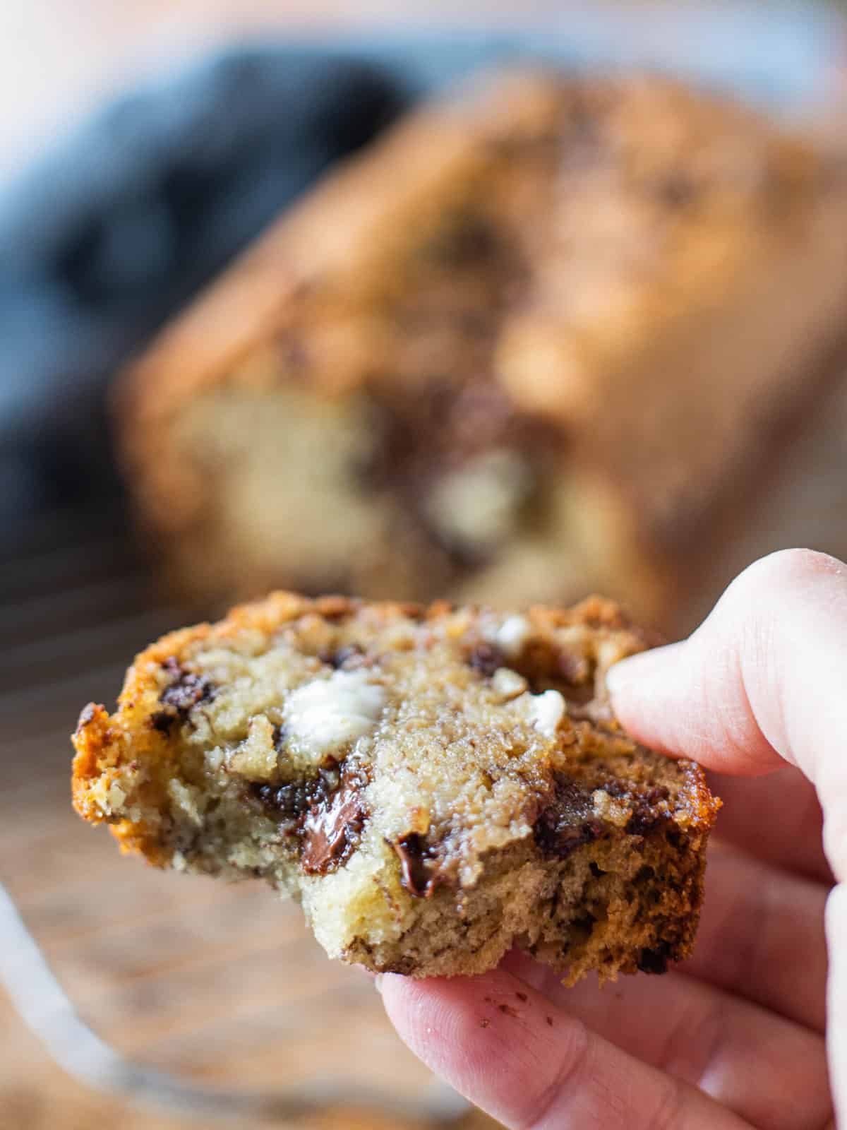 A slice of banana bread broken in half held in a hand with butter and melted chocolate.