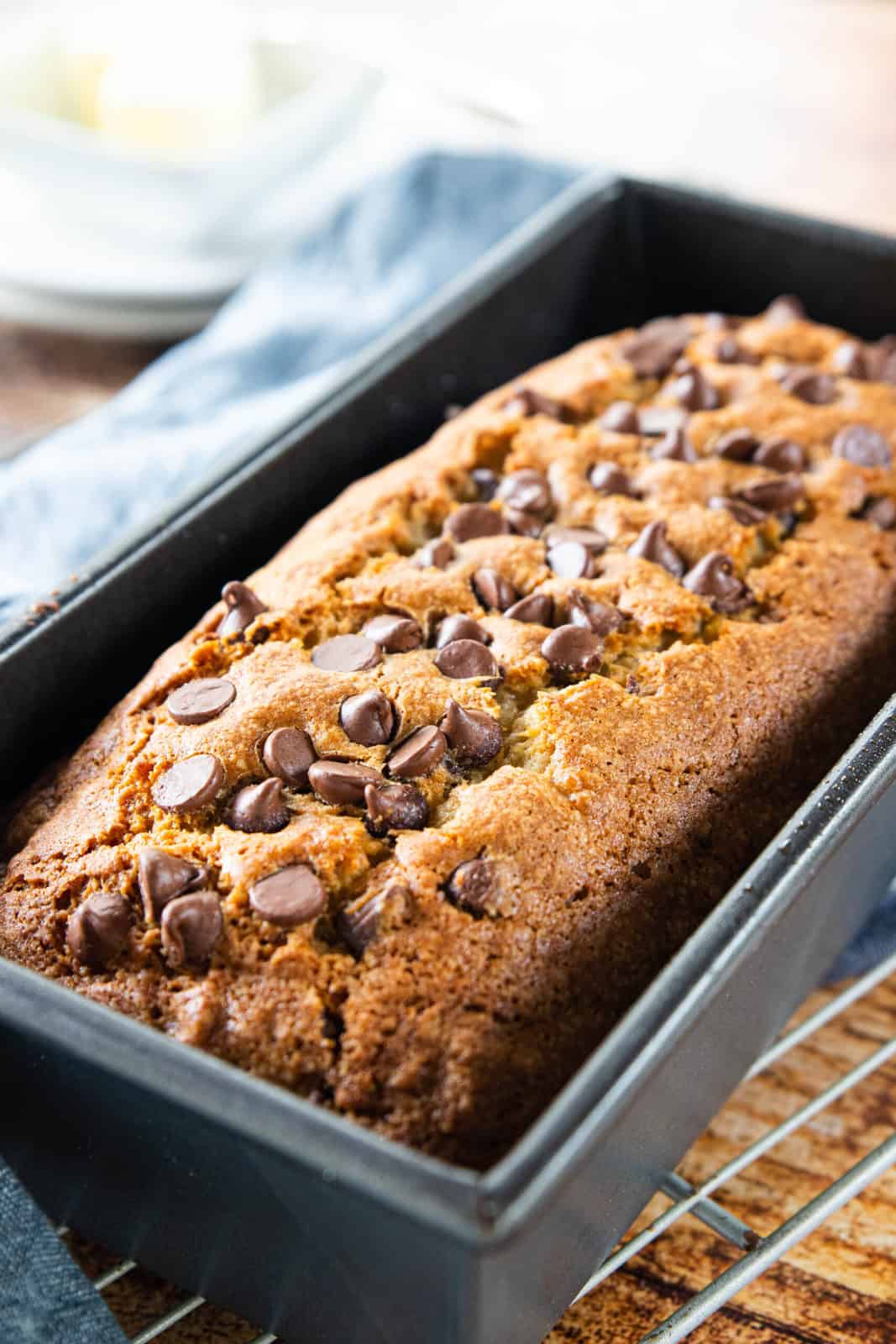 A freshly baked loaf of chocolate chip banana bread shown up close in a bread pan on a cooling rack.