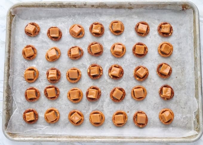 Christmas Pretzel Treats shown on a baking pan with round pretzels lined up with caramels in the centers of them all. 