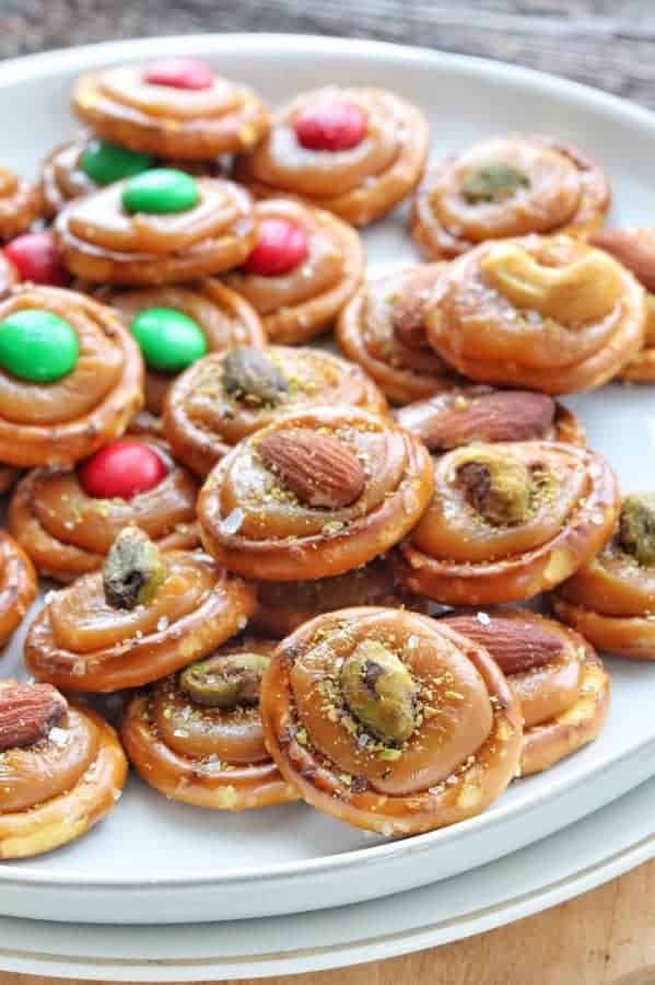 Christmas Pretzels shown with M&M's and pistachios in caramel on a white plate.