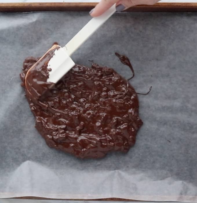 chocolate bark recipe showing melted chocolate mixture being spread with a spatula on wax paper. 