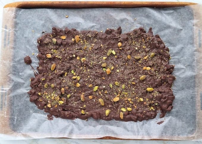 A pan of chocolate bark recipe hardened but not broken yet on wax paper on a baking sheet. 