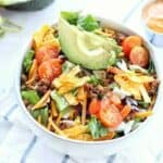 Taco salad shown in a blow with fresh tomatoes and avocado on top.
