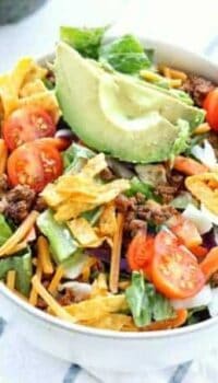 Taco salad shown in a blow with fresh tomatoes and avocado on top.