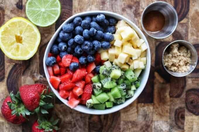 A variety of fruit in a bowl next to a lemon and a lime half.