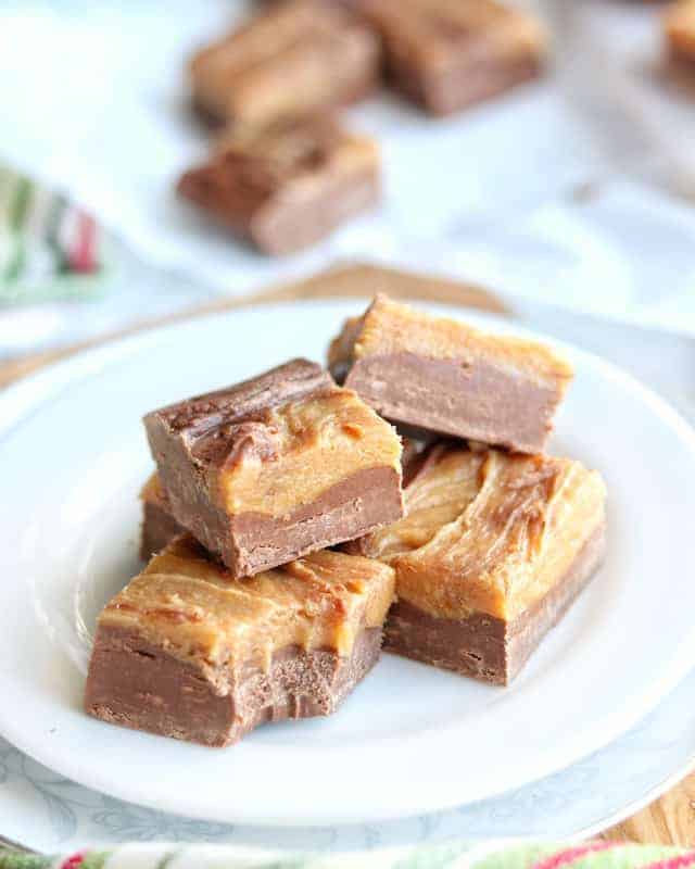Easy Peanut Butter Fudge Recipe an Old Fashioned Fudge made in the microwave shown stacked on a white plate with fudge squares in the background.