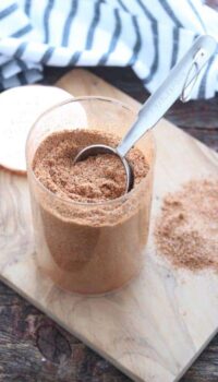 Chicken taco seasoning shown in a clear glass container with a tablespoon removing some.