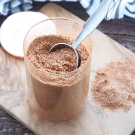 Chicken taco seasoning shown in a clear glass container with a tablespoon removing some.