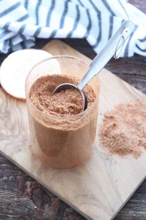 Chicken taco seasoning shown in a clear glass container with a tablespoon removing some.