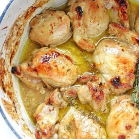 Chicken thighs in a white pot in a liquid with fresh herbs.