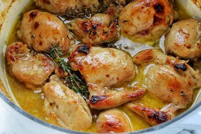 Boneless Skinless Chicken thighs stovetop shown in a white pot. Chicken thighs are browned and shown in juice with fresh herbs.