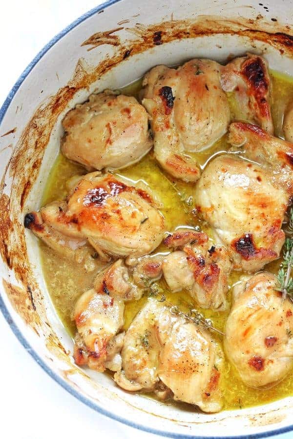 Chicken thighs are browned and shown in juice with fresh herbs.