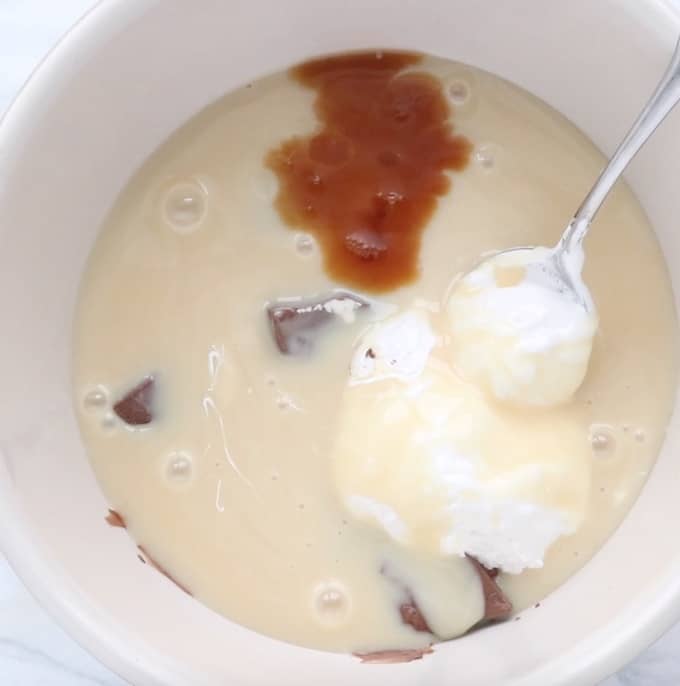 Chocolate, sweetened condensed milk, marshmallow fluff, and vanilla in a white bowl. 