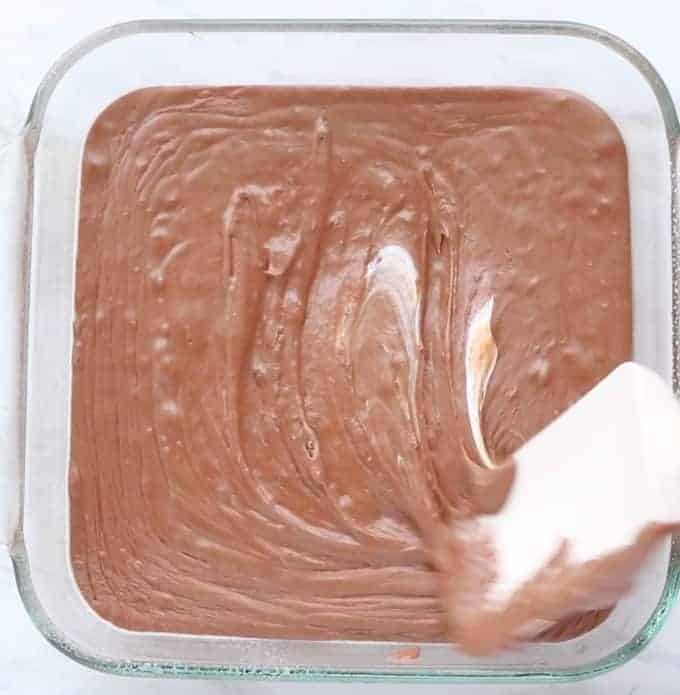 Fudge in a clear 9x9 pan with a spatula spreading the top flat. 