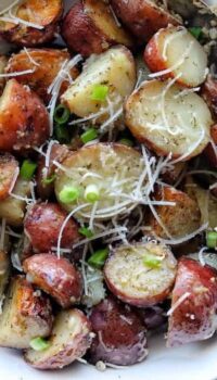 A white bowl with roasted red potatoes sliced in half with shredded parmesan and green onion on top.