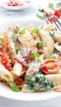 A white bowl with creamy chicken pasta with bacon, tomatoes, and spinach.