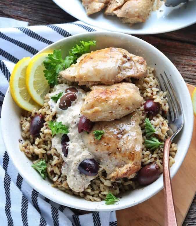 Greek Chicken thighs shown in a white bowl on a bed of rice 