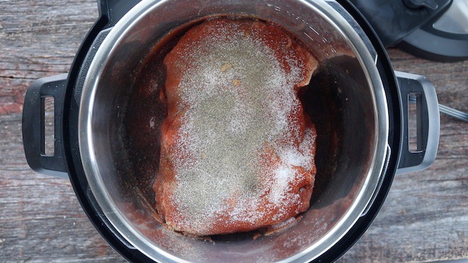 Pulled pork instant pot shown top down with raw pork shoulder shown covered in spices. 