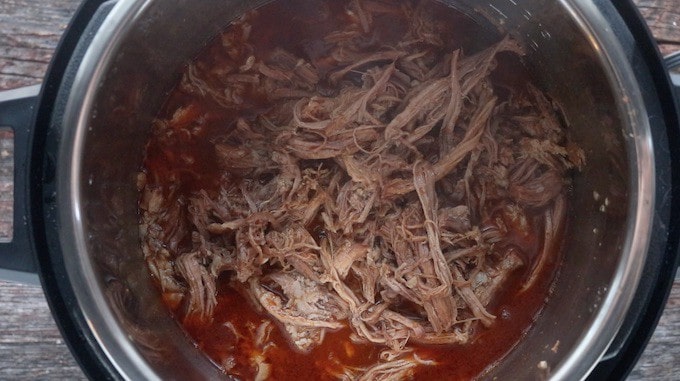 Instant pot pork shown shredded in instant pot after cooking. 