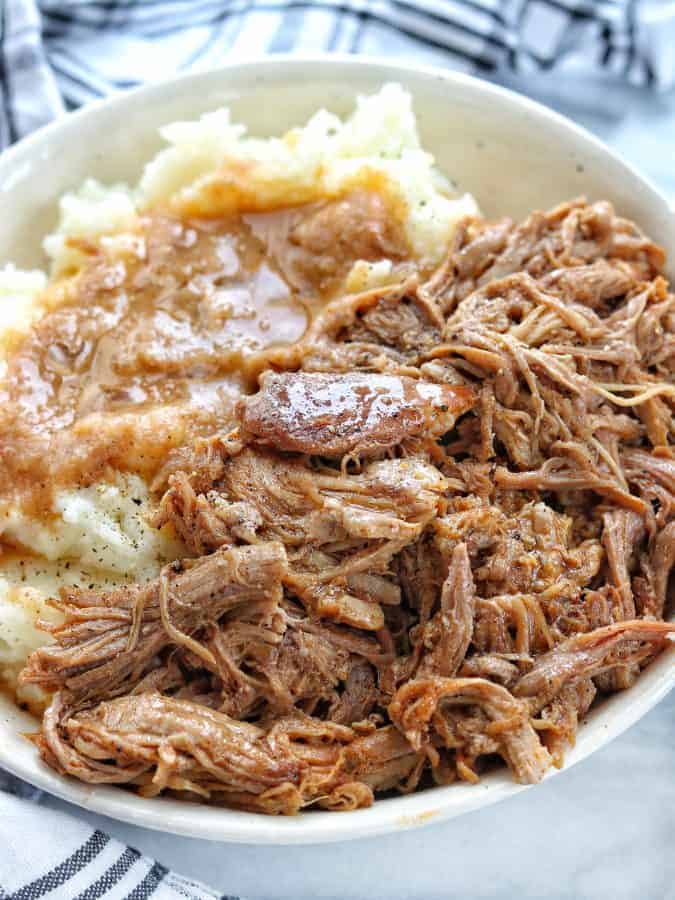 pork roast instant pot shown close up in a white bowl with mashed potatoes and gravy on white marble surface. 