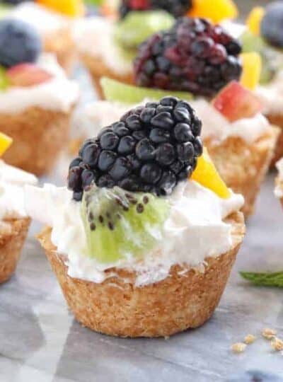 Mini Tarts a mini fruit tart recipe shown on white marble with a fresh blackberry on top with kiwi and peach.