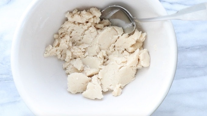 Mini tarts recipe being made showing the crust ingredients blended into a stiff dough in a white bowl with a spoon.