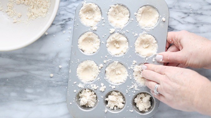 Mini Tart recipe dough being added to mini muffin tins with 2 hands on a white pastry board.