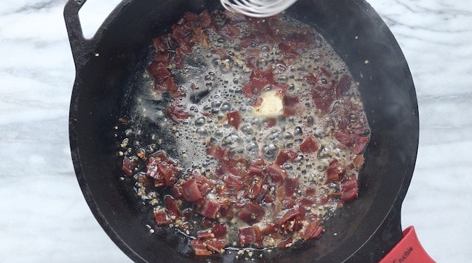 Creamy Chicken and Bacon Pasta recipe being made, showing bacon, garlic, and melting butter in a black cast iron pan.