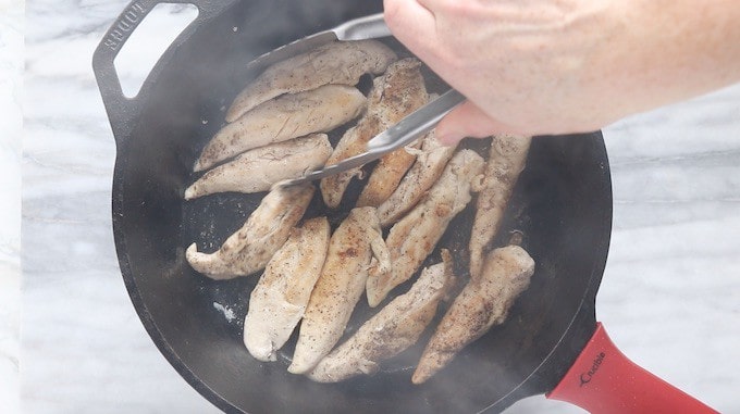 Creamy Chicken and Bacon Pasta recipe being made. Showing chicken tenders in a black cast iron pan being turned with a metal spatula.