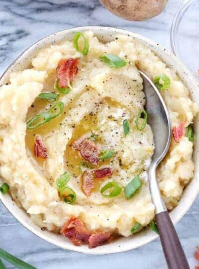 A bowl of colcannon is shown in a white bowl topped with bacon, butter, and green onions.