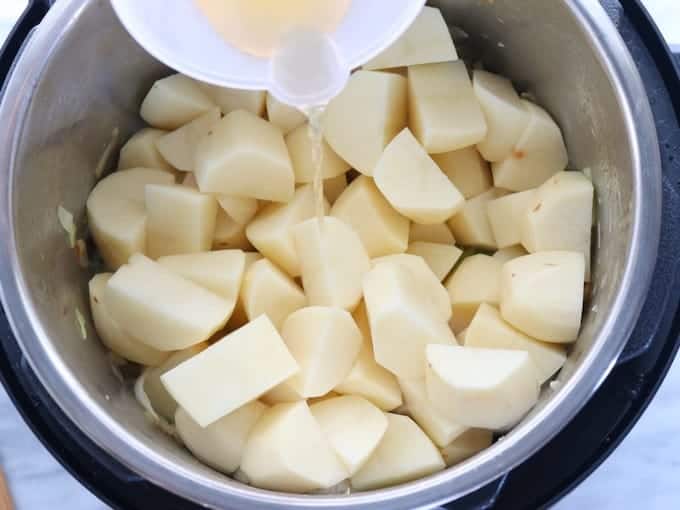 Irish potato and cabbage dish shown being made in an instant pot with potatoes and broth added.