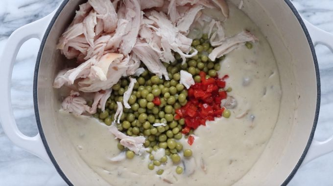  rotisserie chicken, peas, and pimentos are added to the creamy chicken a la king that's in a white stockpot.