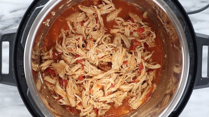 Instant pot Mexican chicken tacos shown in a pressure cooker after being cooked and shredded.