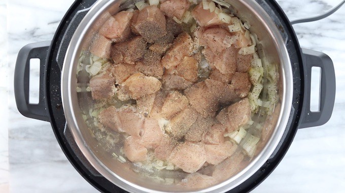 Instant pot chicken stew a pressure cooker soup recipe being made showing top down into instant pot chicken and onions being sautéed with spices. 