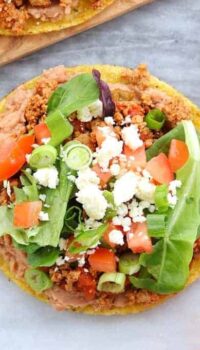 A tostada is loaded with refried beans, turkey taco meat, lettuce, tomatoes, and cheese.