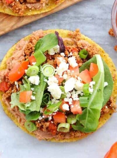 A tostada is loaded with refried beans, turkey taco meat, lettuce, tomatoes, and cheese.