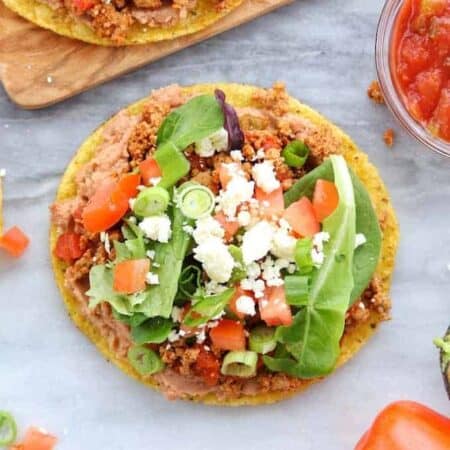 A tostada is loaded with refried beans, turkey taco meat, lettuce, tomatoes, and cheese.