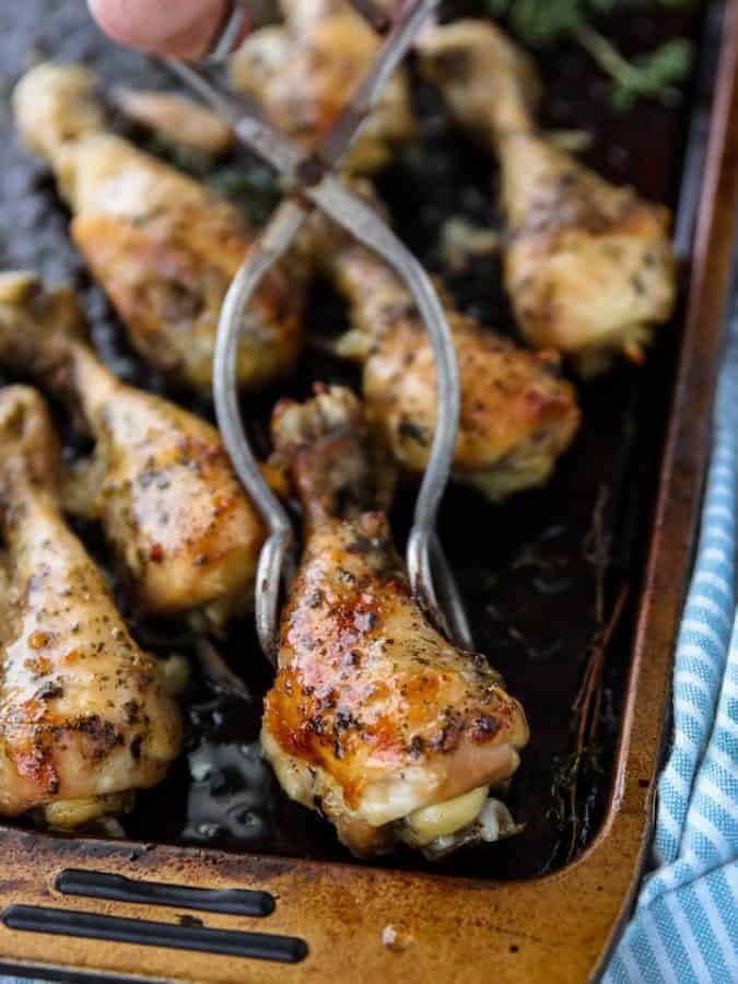 Crockpot Chicken Legs, a flavorful chicken recipe being shown on a black baking sheet with a pair of tons holding a single chicken leg.