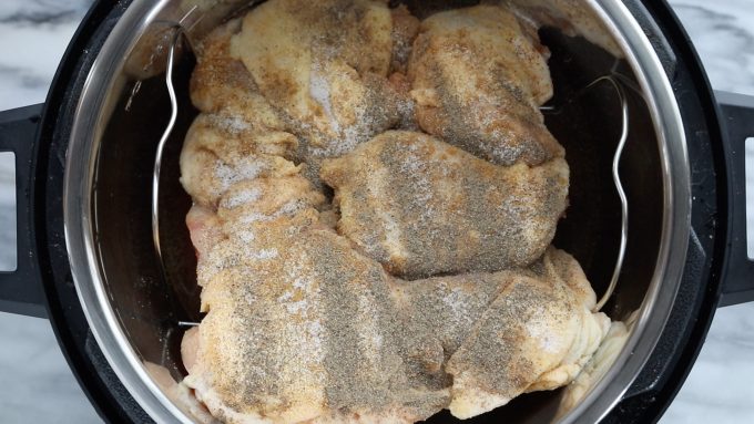 Instant Pot Frozen Chicken Thighs showing raw, frozen chicken with broth and spices on top of chicken in the Instant Pot on the Instant Pot rack. 