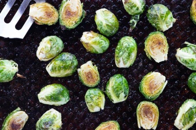 Baked Brussels sprouts, an oven roasted vegetable recipe being shown on a black baking sheet with a metal spatula 